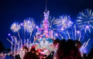Castillo de Disneyland Paris iluminado con fuegos artificiales nocturnos.