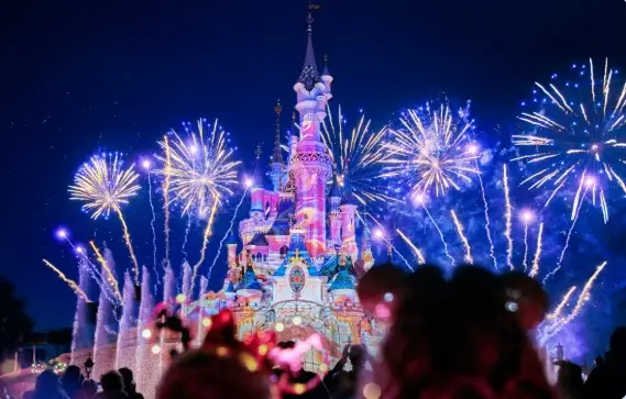 Castillo de Disneyland Paris iluminado con fuegos artificiales nocturnos.